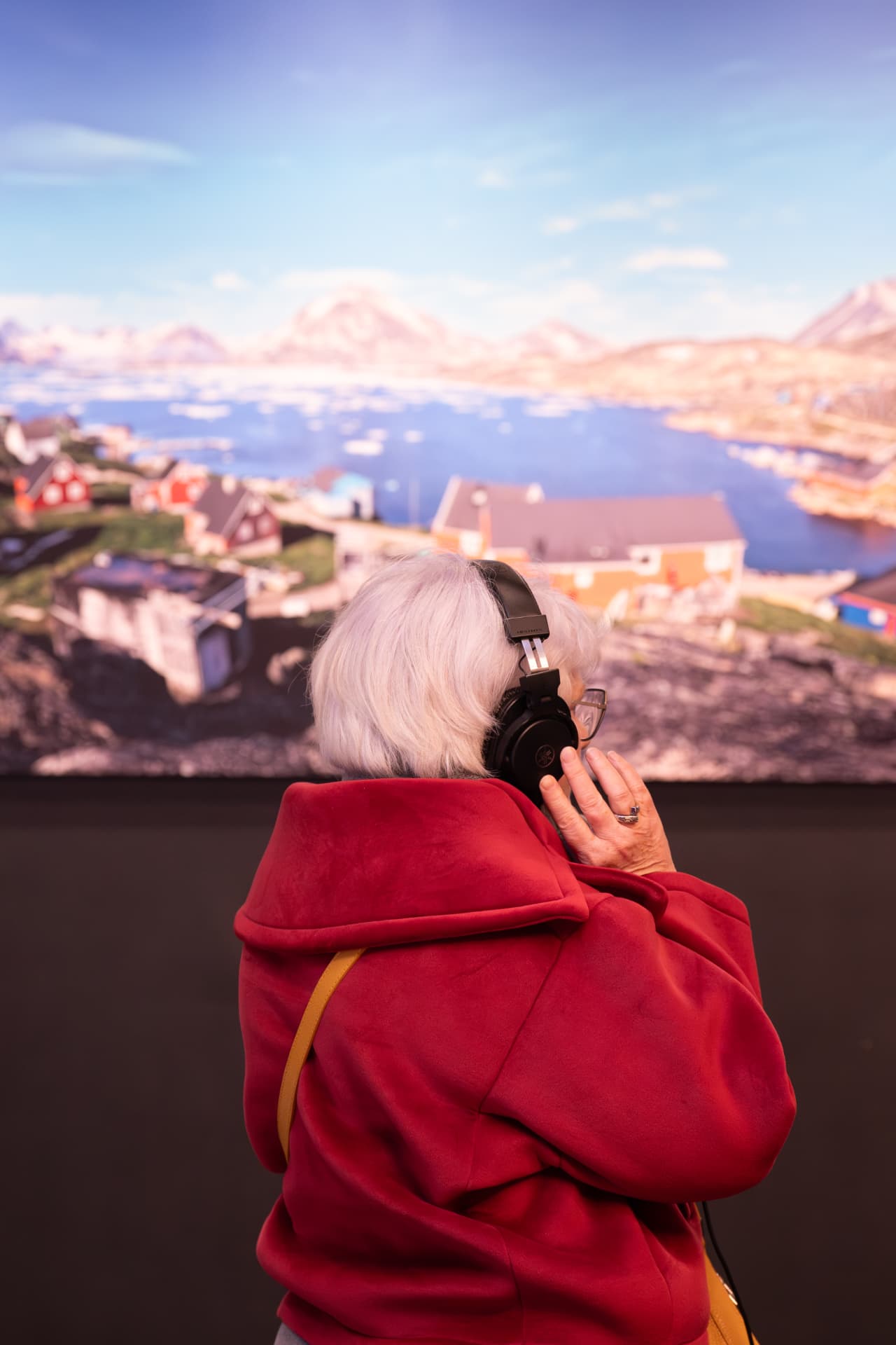 Une visiteuse au casque écoute une installation sonore face à une projection immersive d'un village groenlandais